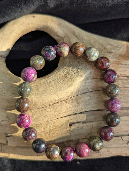 Atlantisite round bead stretch bracelet positioned on a neutral presentation surface, demonstrating bead uniformity and the stark contrast between green serpentine and purple stichtite.