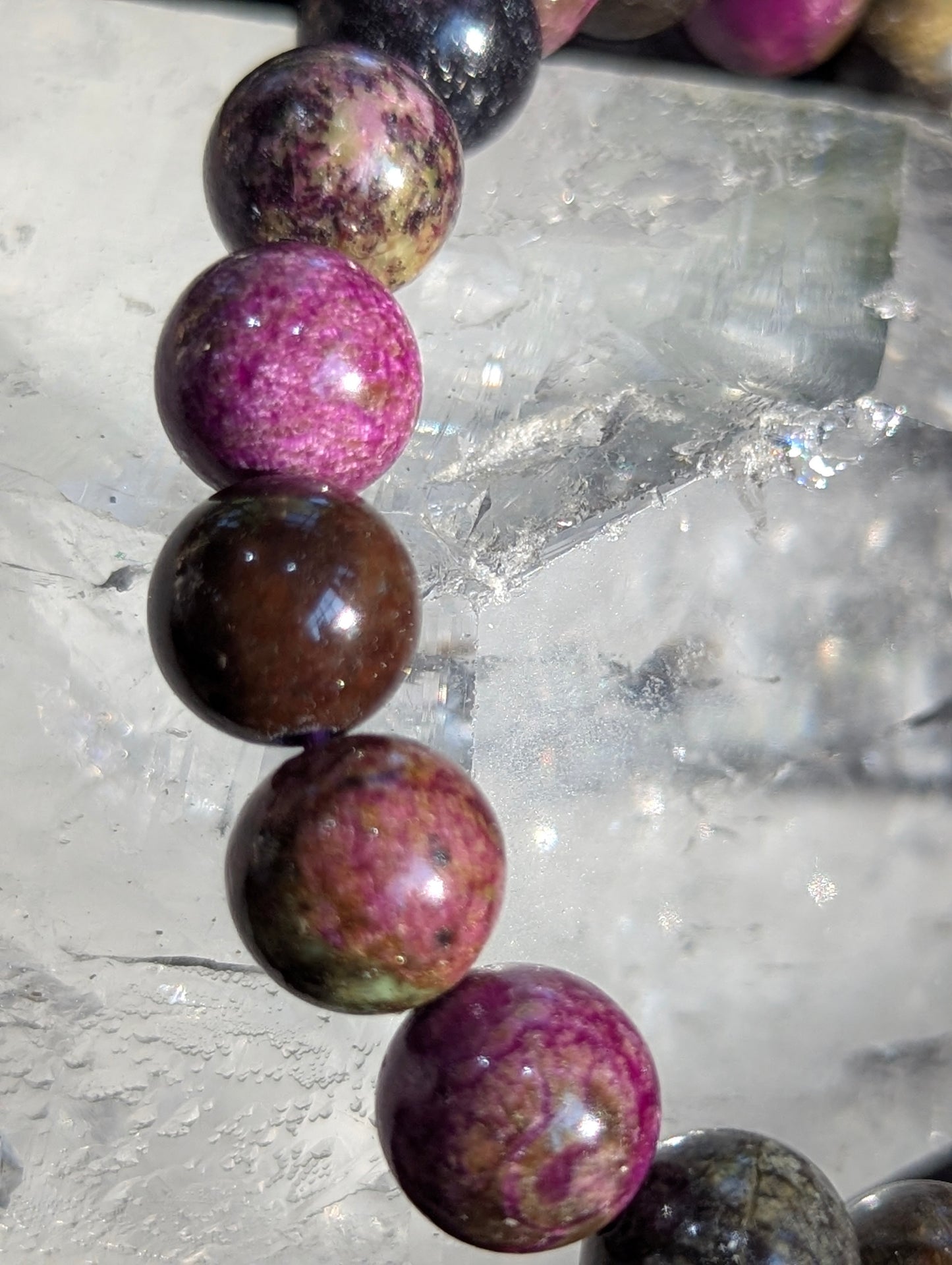 Macro close-up view of polished 9.5mm Atlantisite spheres, highlighting the dense, waxy luster of the serpentine matrix intersected by deep violet stichtite inclusions.