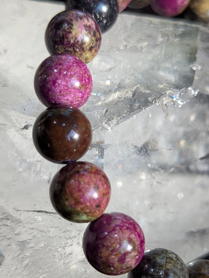 Macro close-up view of polished 9.5mm Atlantisite spheres, highlighting the dense, waxy luster of the serpentine matrix intersected by deep violet stichtite inclusions.