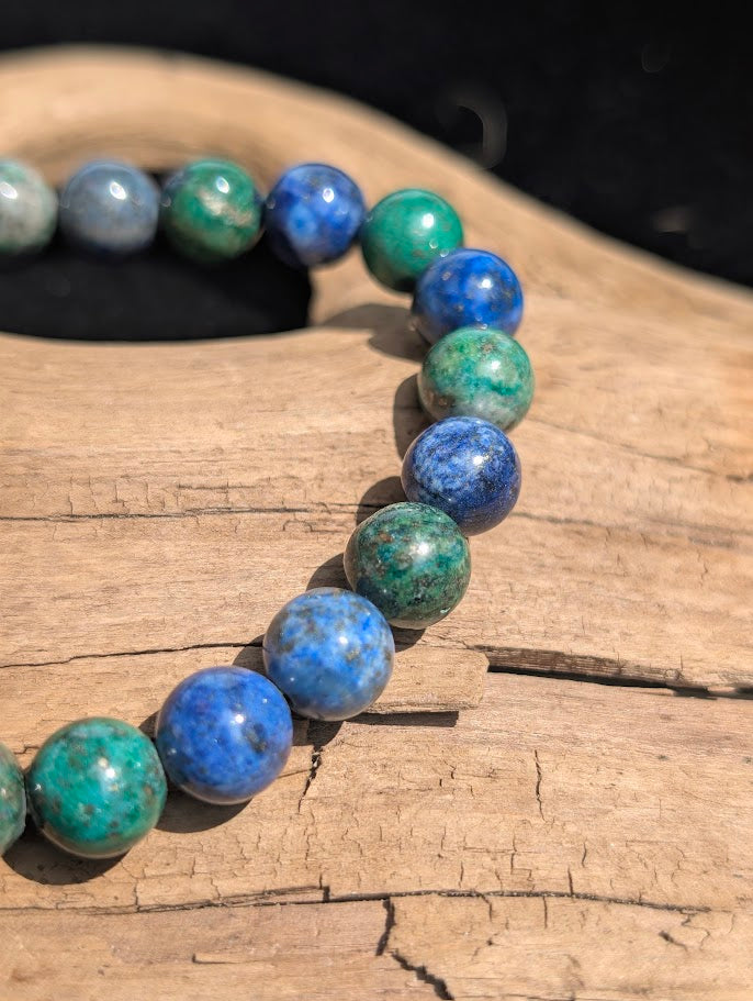 Macro view of polished 8mm Azurite-Malachite spherical beads on driftwood, displaying the natural mottling of blue and green copper carbonates.