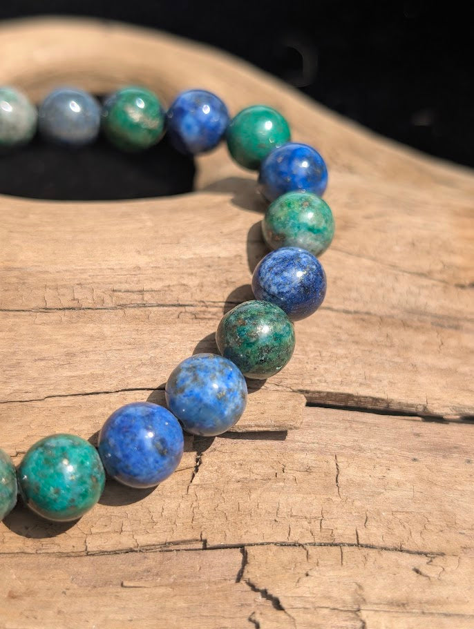 Close-up of a polished 8mm Azurite-Malachite stretch bracelet resting on natural wood in bright sunlight.