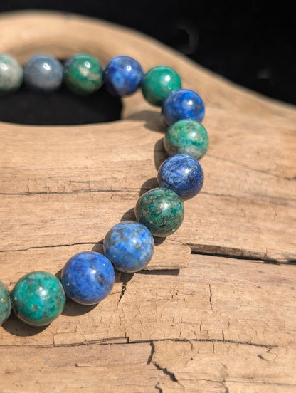 Close-up of a polished 8mm Azurite-Malachite stretch bracelet resting on natural wood in bright sunlight.