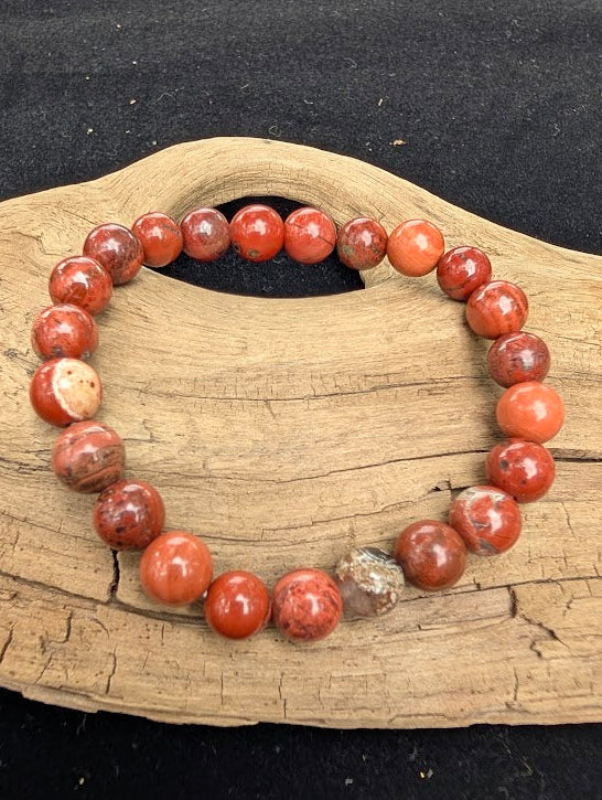 8mm polished Banded Red Jasper beaded stretch bracelet resting on a driftwood display, showing earthy red tones and dark striping.