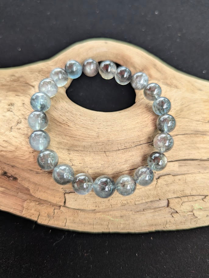 Intuitively selected 9mm AAA Grade Brazilian Black Devil Aquamarine beaded stretch bracelet resting on driftwood, showing smooth spherical polish and balanced colour matrix.