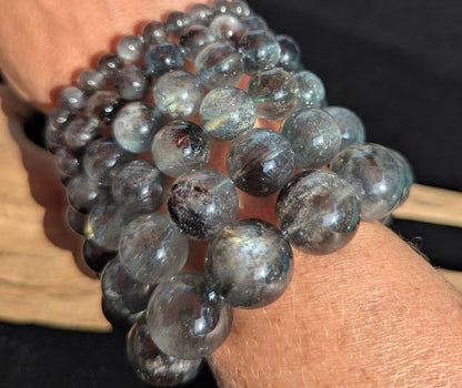 Macro close-up of stacked Brazilian Black Devil Aquamarine beaded bracelets on a wrist, highlighting the high vitreous lustre and smoky grey-blue beryl matrix.
