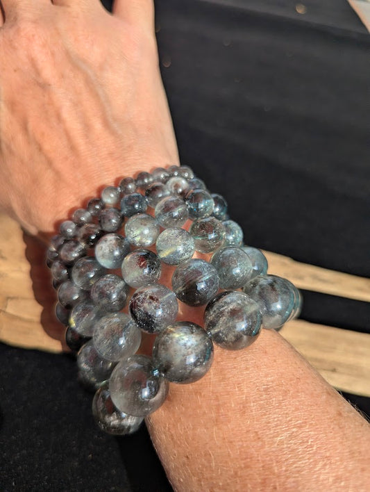 Stack of Brazilian Girasol Black Devil Aquamarine bracelets illuminated in direct sunlight, showcasing the reflective silver chatoyancy rolling across the beads.