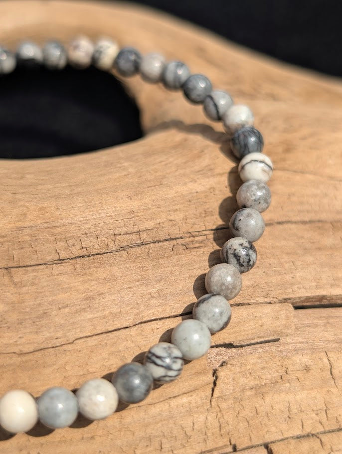 Macro view of polished 4mm Black Network Stone spherical beads on driftwood, highlighting the natural black spiderweb veining on a light grey base.