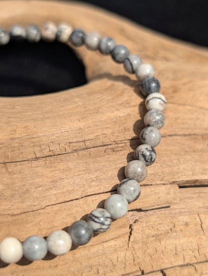 Macro view of polished 4mm Black Network Stone spherical beads on driftwood, highlighting the natural black spiderweb veining on a light grey base.