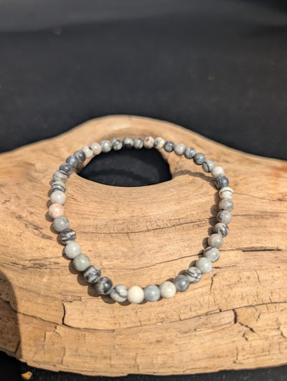 A 4mm Black Network Stone beaded bracelet resting on natural driftwood, displaying a high-contrast black and white matrix.