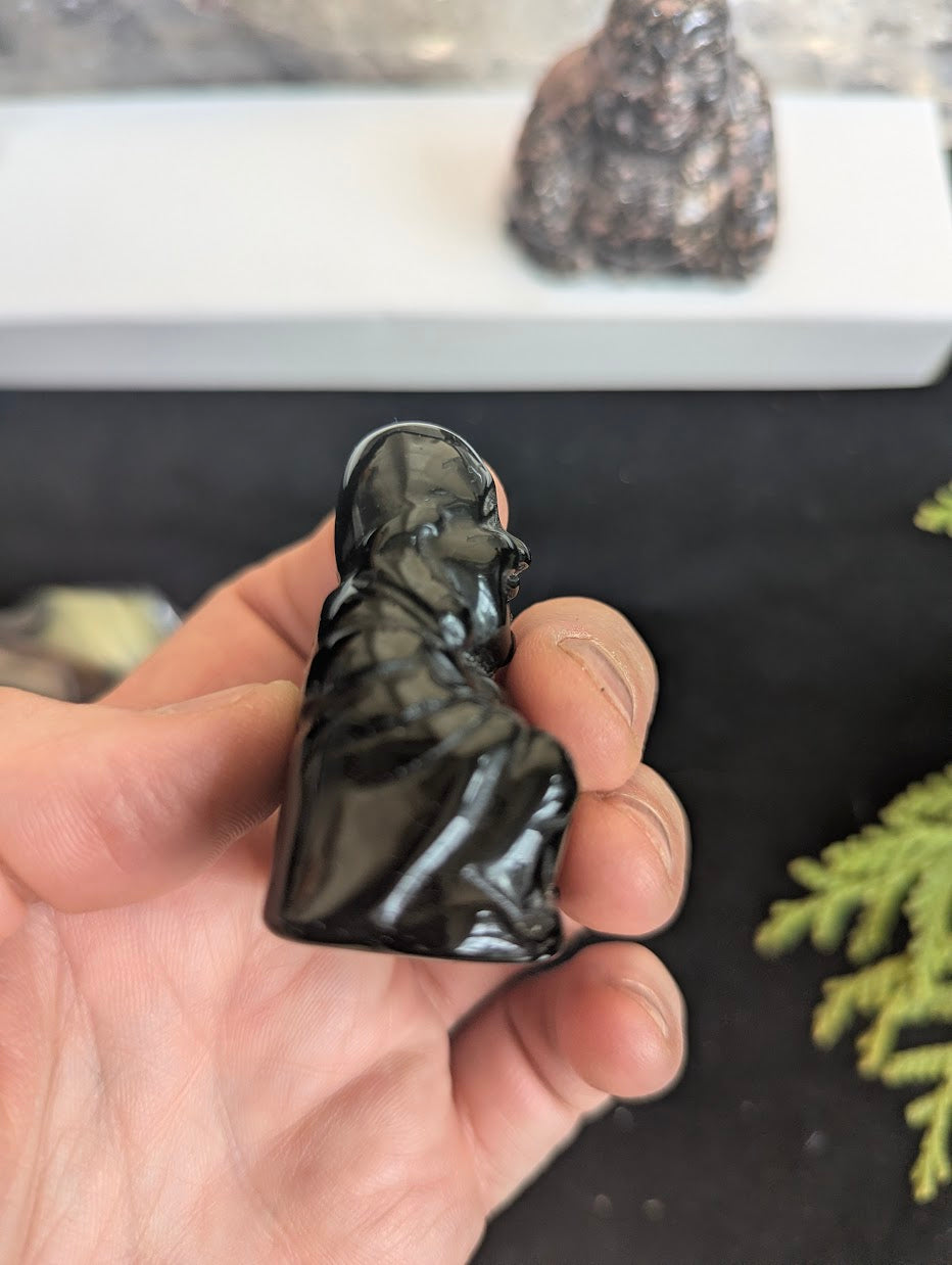 Angled view of a Black Obsidian Buddha carving emphasizing the smooth volcanic glass texture and high-gloss polish.