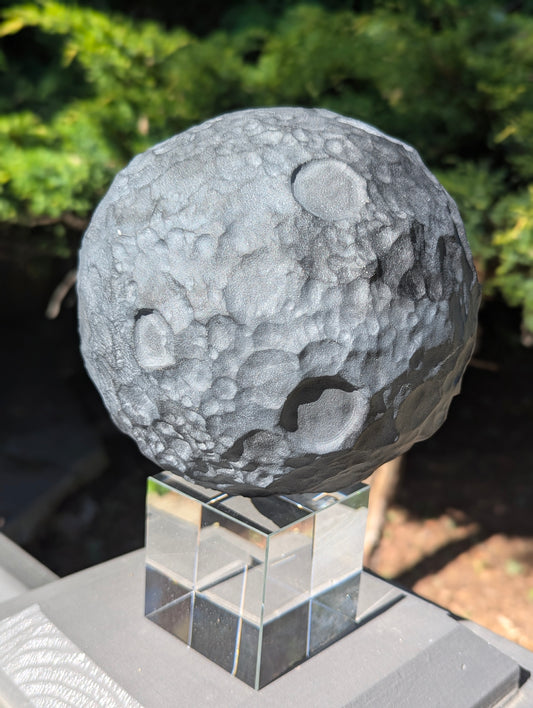 A large 160 mm (6.30 in) Black Obsidian carved moon sphere resting on a clear acrylic stand outdoors.