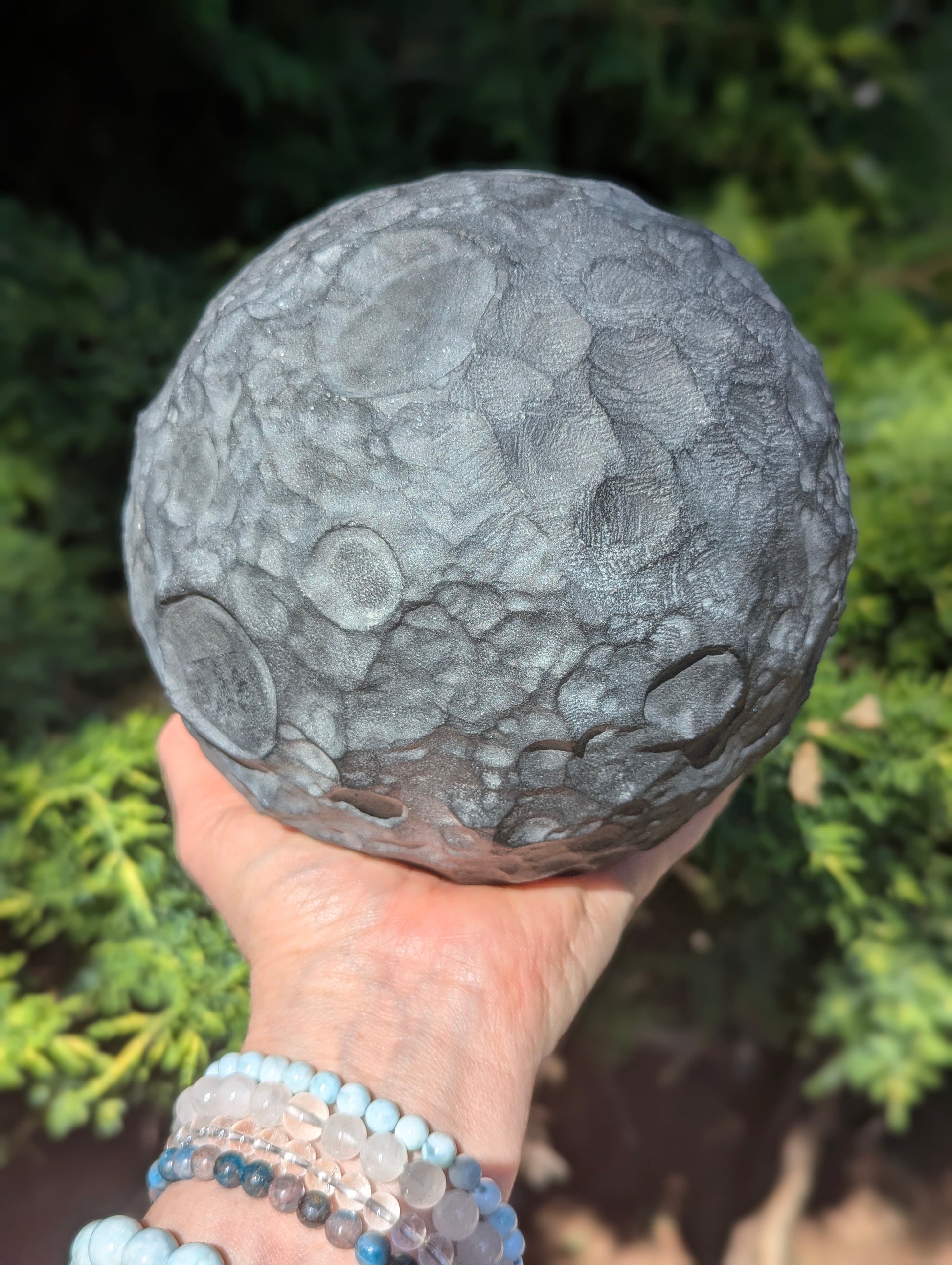 A massive 4.7 kg Black Obsidian carved moon sphere held in a hand, demonstrating its substantial size and matte finish in sunlight.