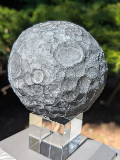 Close-up of a 160 mm (6.30 in) Black Obsidian moon sphere showing heavily textured, hand-carved lunar craters.