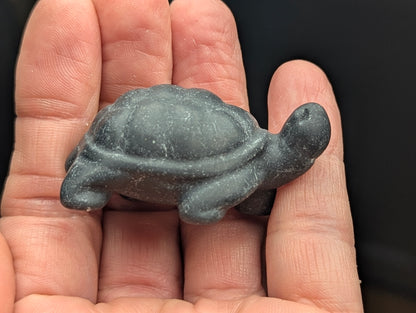 Side profile of a polished Black Obsidian crystal tortoise carving resting on an open palm, highlighting smooth shell contours and sculpted limbs.