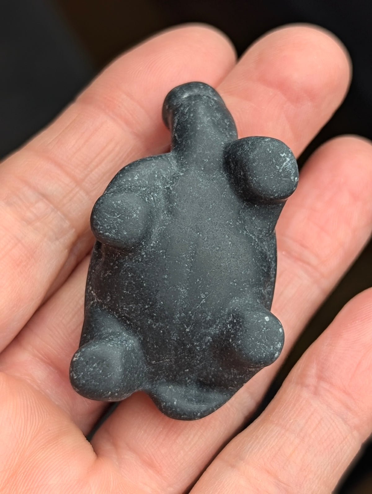 Underside view of a Black Obsidian crystal tortoise carving resting in an open hand, showing sculpted legs and smooth belly polish.