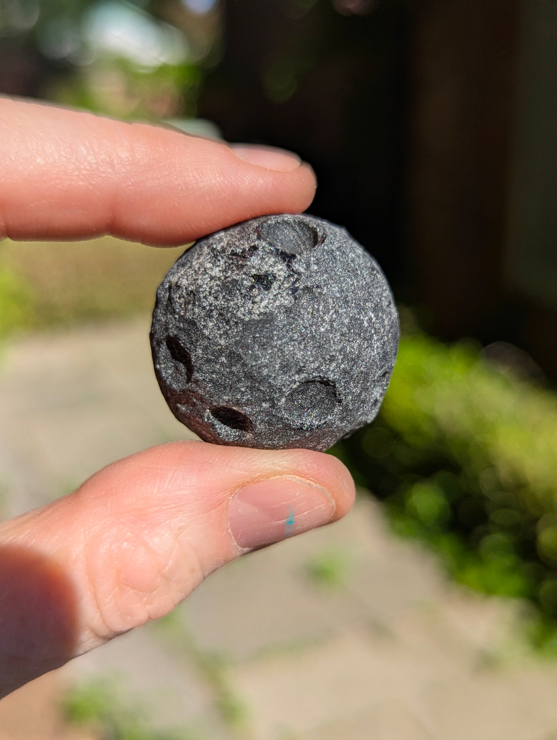 Close-up of a 30 mm (1.18 in) Black Obsidian mini carved moon held between two fingers, highlighting the unpolished crater textures.