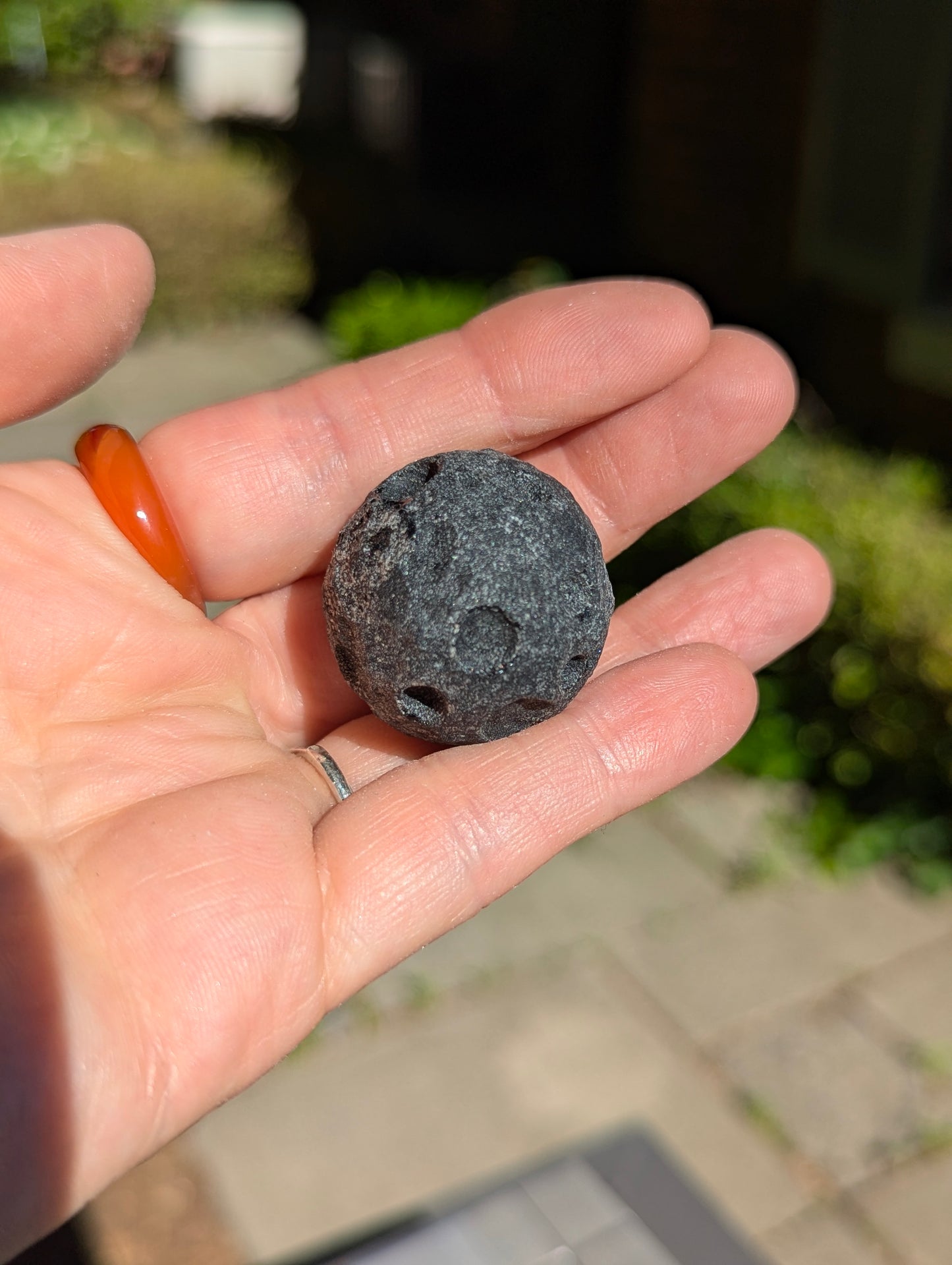 A 30 mm (1.18 in) Black Obsidian mini carved moon resting in the palm of a hand in natural outdoor lighting.