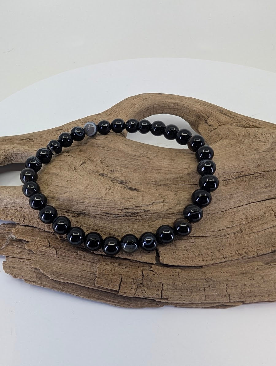 6mm Black Onyx bead bracelet displayed on natural wood showing high-polish luster and deep black color.