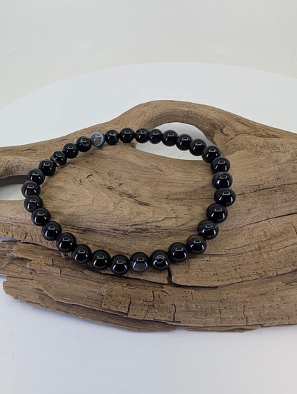 6mm Black Onyx bead bracelet displayed on natural wood showing high-polish luster and deep black color.