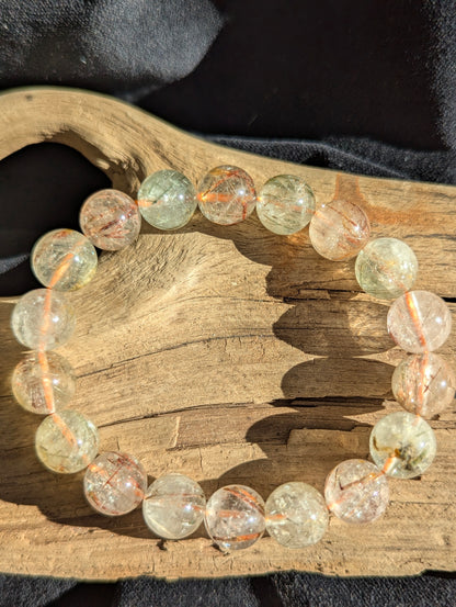 A 12mm bead stretch bracelet featuring vivid copper and black rutile needle inclusions suspended within a flawless transparent quartz matrix from Brazil