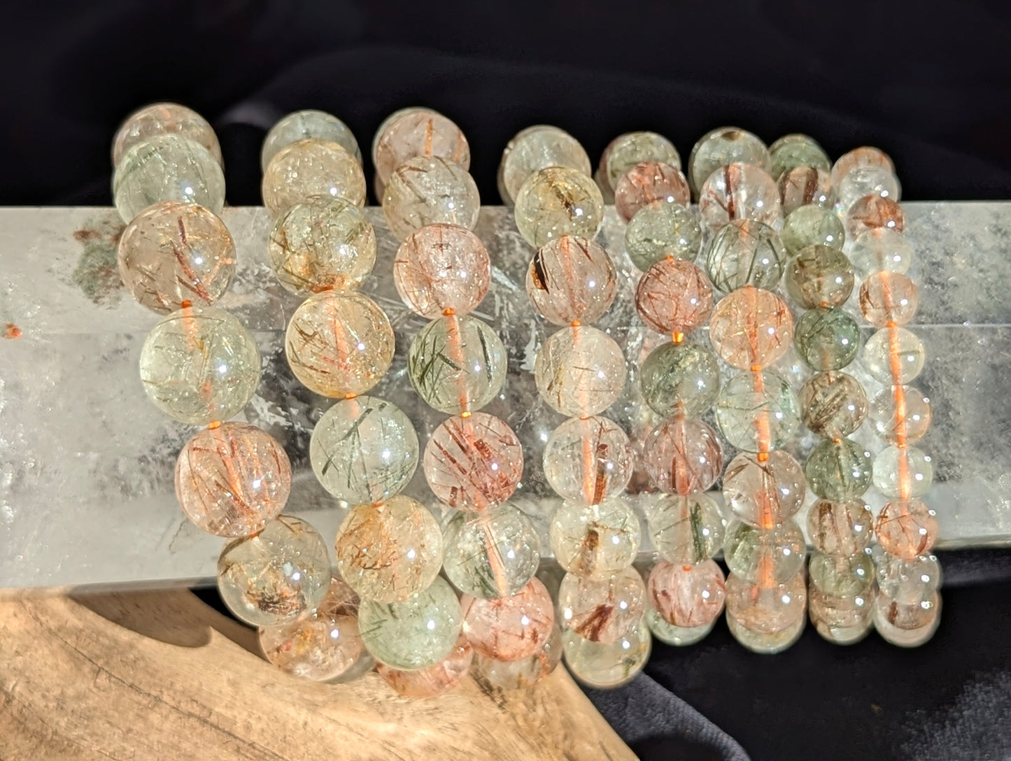 Stacked display of AA-grade Brazilian black and red copper rutilated quartz stretch bracelets showcasing varying bead sizes and high-clarity polish.
