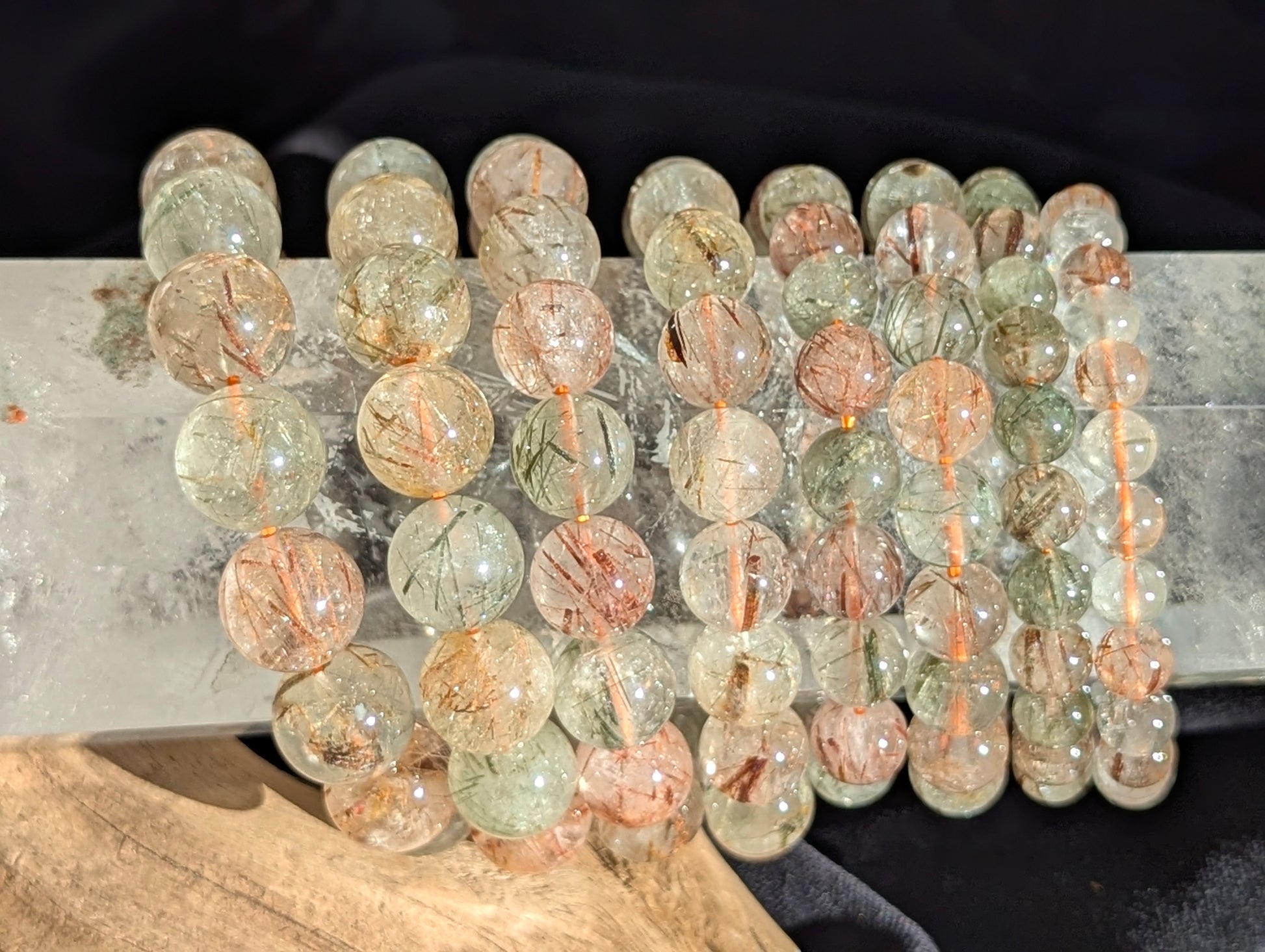 Stacked display of AA-grade Brazilian black and red copper rutilated quartz stretch bracelets showcasing varying bead sizes and high-clarity polish.