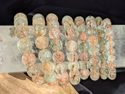 Stacked display of AA-grade Brazilian black and red copper rutilated quartz stretch bracelets showcasing varying bead sizes and high-clarity polish.