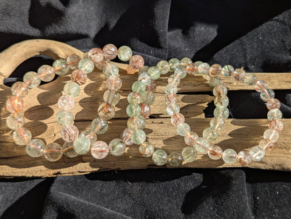 Stacked display of AA-grade Brazilian black and red copper rutilated quartz stretch bracelets showcasing varying bead sizes and high-clarity polish.
