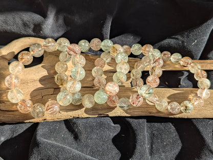 Stacked display of AA-grade black and red copper rutilated quartz stretch bracelets showcasing varying bead sizes and high-clarity polish.