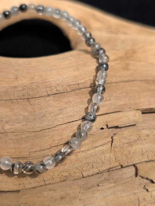 Macro view of polished 4mm Black Rutilated Quartz spherical beads on driftwood, highlighting the internal black tourmaline (schorl) needles.