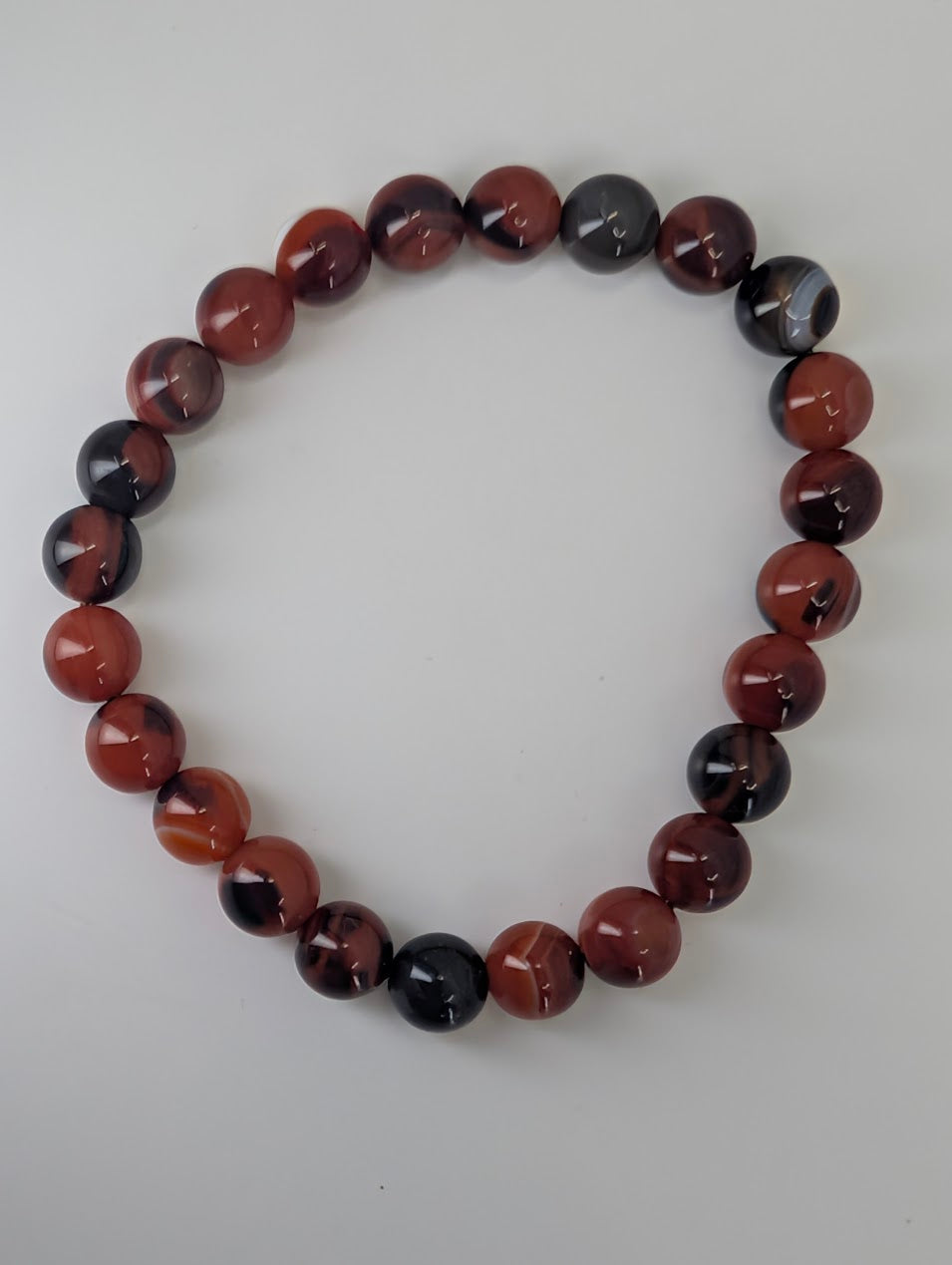 Overhead view of Black Sardonyx bracelet arranged in a circle on white background