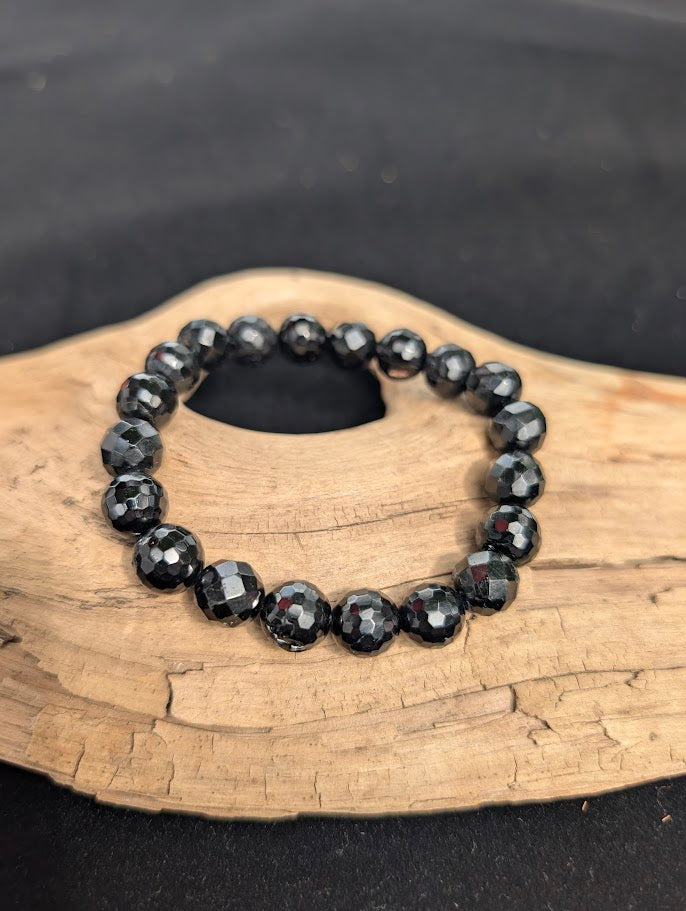 10mm faceted Black Tourmaline beaded stretch bracelet resting on a driftwood display.