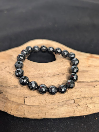 10mm faceted Black Tourmaline beaded stretch bracelet resting on a driftwood display.