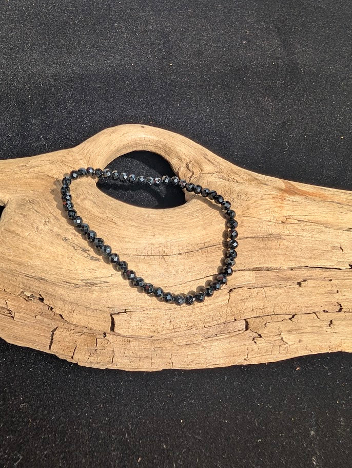 3mm faceted Black Tourmaline beaded stretch bracelet resting on a driftwood display, showing reflective cuts.