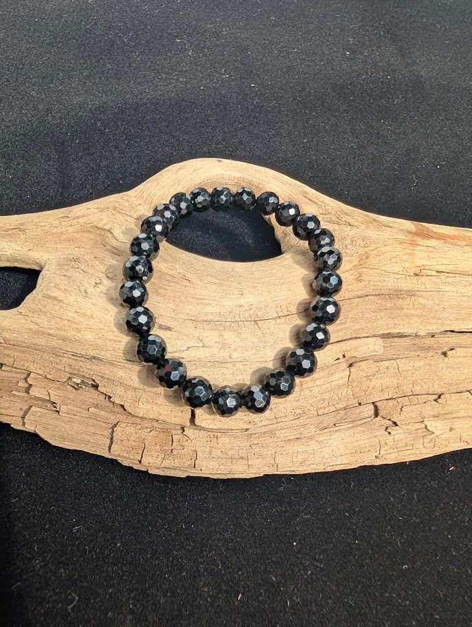 8mm faceted Black Tourmaline beaded stretch bracelet resting on a driftwood display.