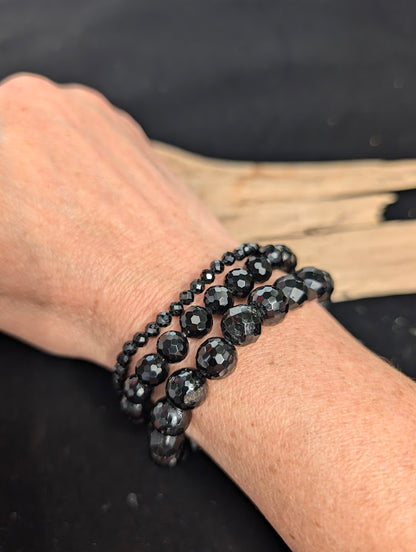 Stack of 3mm, 8mm, and 10mm faceted Black Tourmaline beaded stretch bracelets worn on a wrist for size scale.