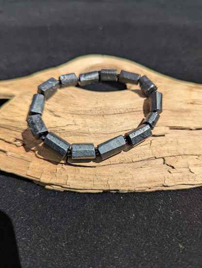 Polished Black Tourmaline geometric prism stretch bracelet resting on a driftwood display, showing a deep black, metallic luster.