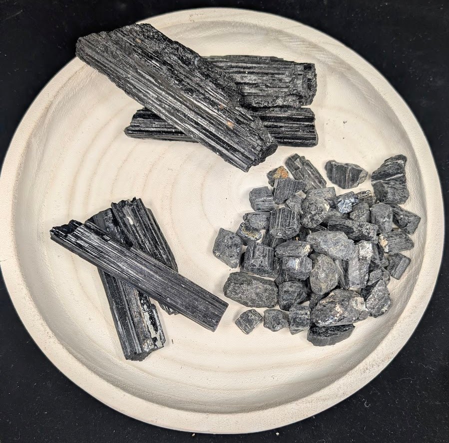 Assorted sizes of raw Black Tourmaline (Schorl) including large rods, small specimens, and loose pieces on a white plate.
