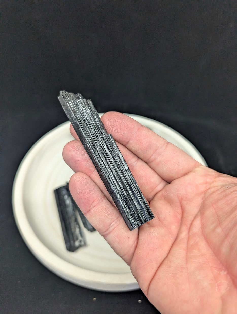 Handheld view of a 10cm Black Tourmaline rod highlighting the reflective ridges and structural integrity.