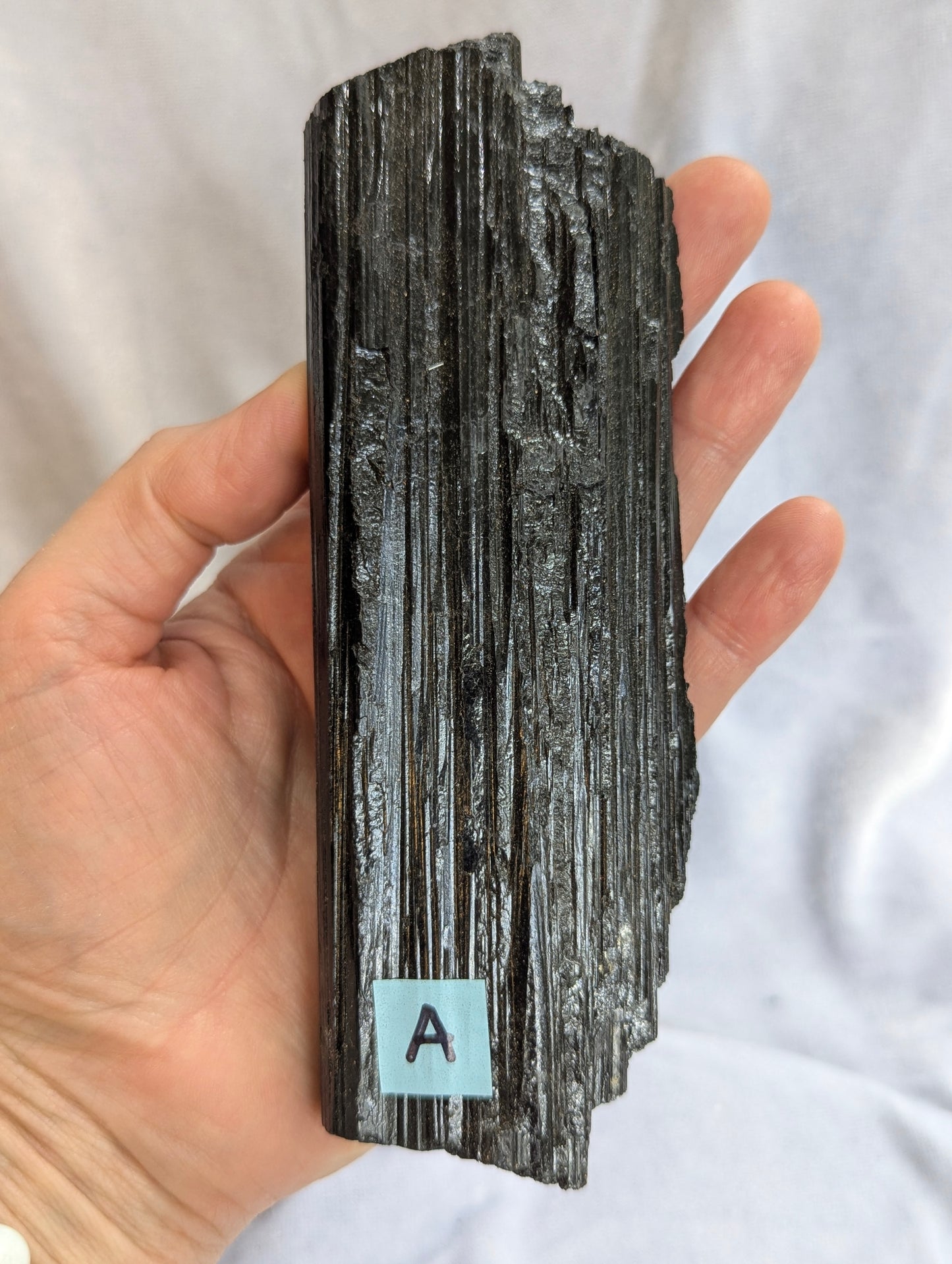 Hand held view of 390g raw Black Tourmaline tower showing natural termination.