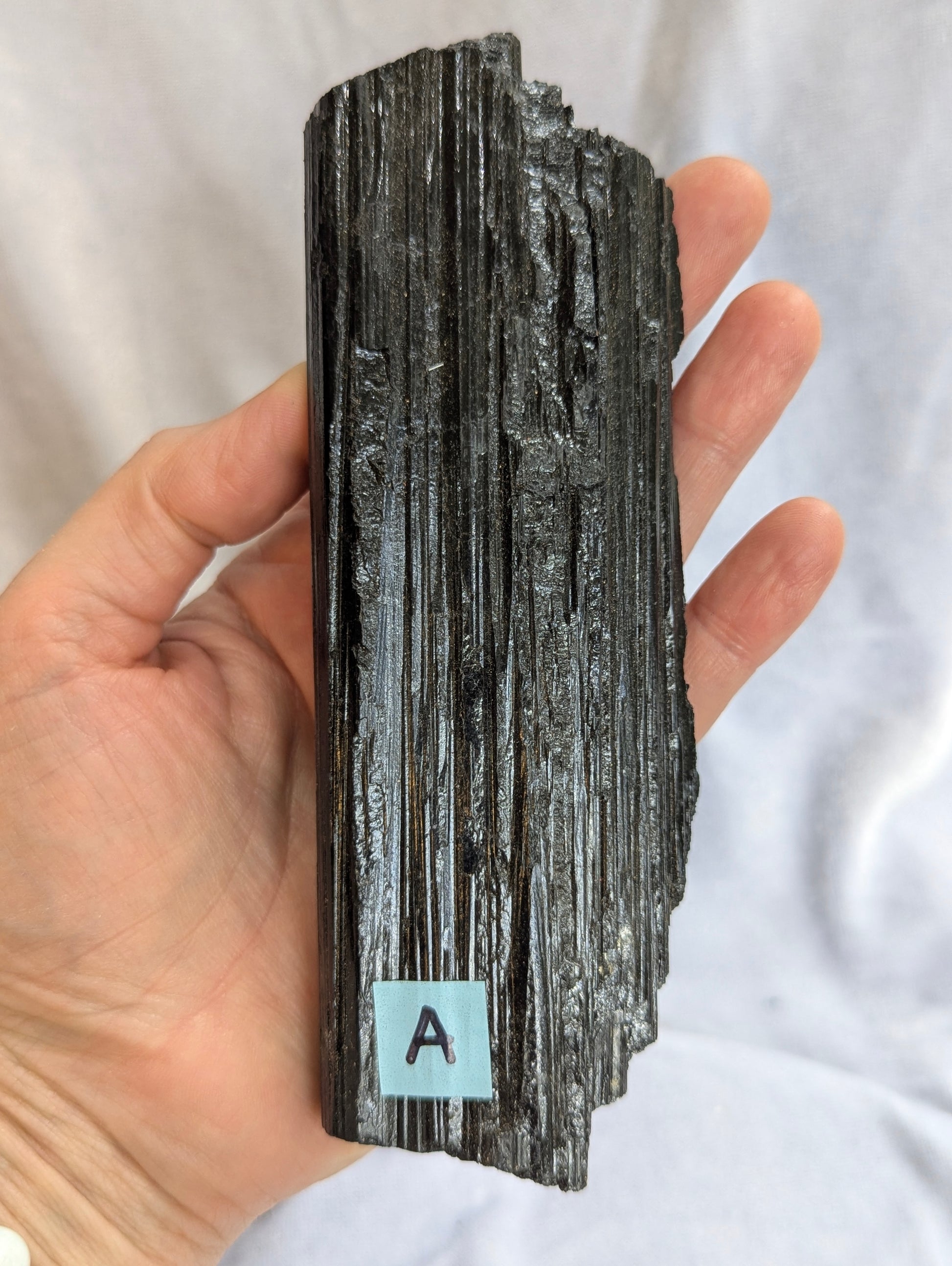 Hand held view of 390g raw Black Tourmaline tower showing natural termination.