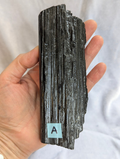 Hand held view of 390g raw Black Tourmaline tower showing natural termination.