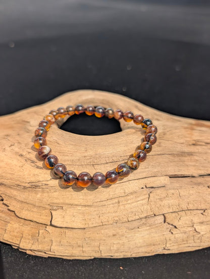 A 6mm Mexican Blue Amber beaded bracelet resting on natural driftwood, displaying its natural golden-brown and cognac colours in standard lighting.