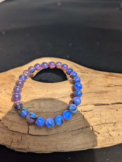 A 7mm Mexican Blue Amber beaded bracelet reacting to UV light, shifting from brown to a brilliant, glowing blue.