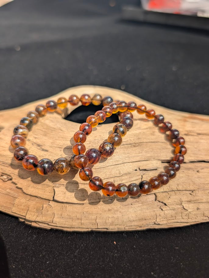Both 6mm and 7mm Mexican Blue Amber beaded bracelets displayed together on driftwood to compare bead sizes.
