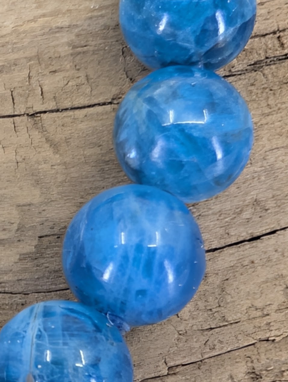 Macro close-up of Blue Apatite beads showing natural internal veils, vitreous luster, and oceanic color zoning.