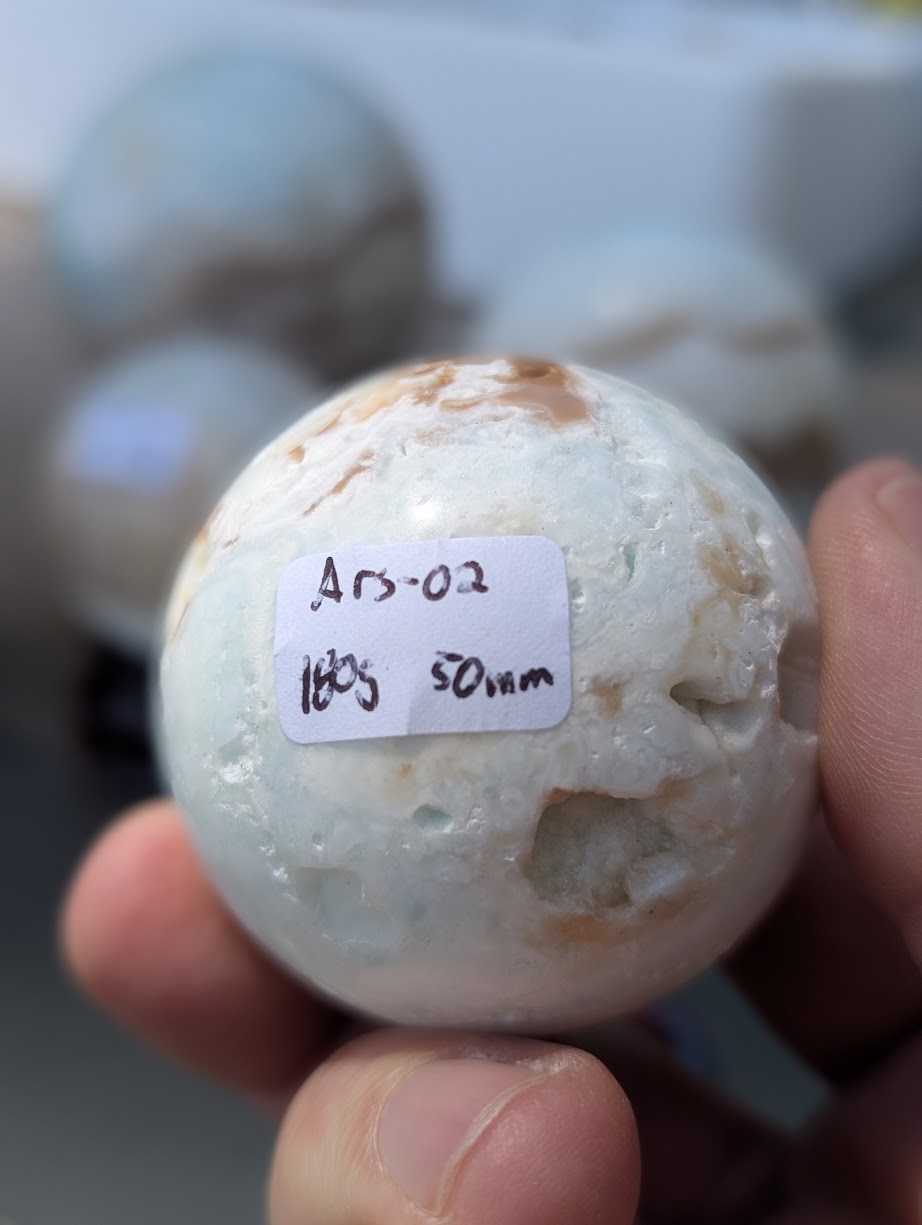 Base view of the 50mm Blue Aragonite sphere held in hand, showing the 180g weight label for variant Ars-02.