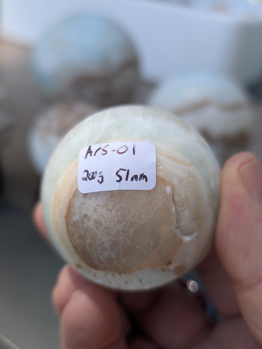 Base view of the 51mm Blue Aragonite sphere held in hand, showing the 200g weight label for variant Ars-01.