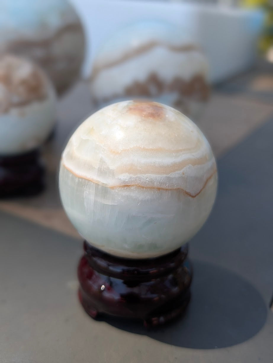 Front view of the 51mm Blue Aragonite sphere showing thick, sweeping white and tan polished aragonite bands.