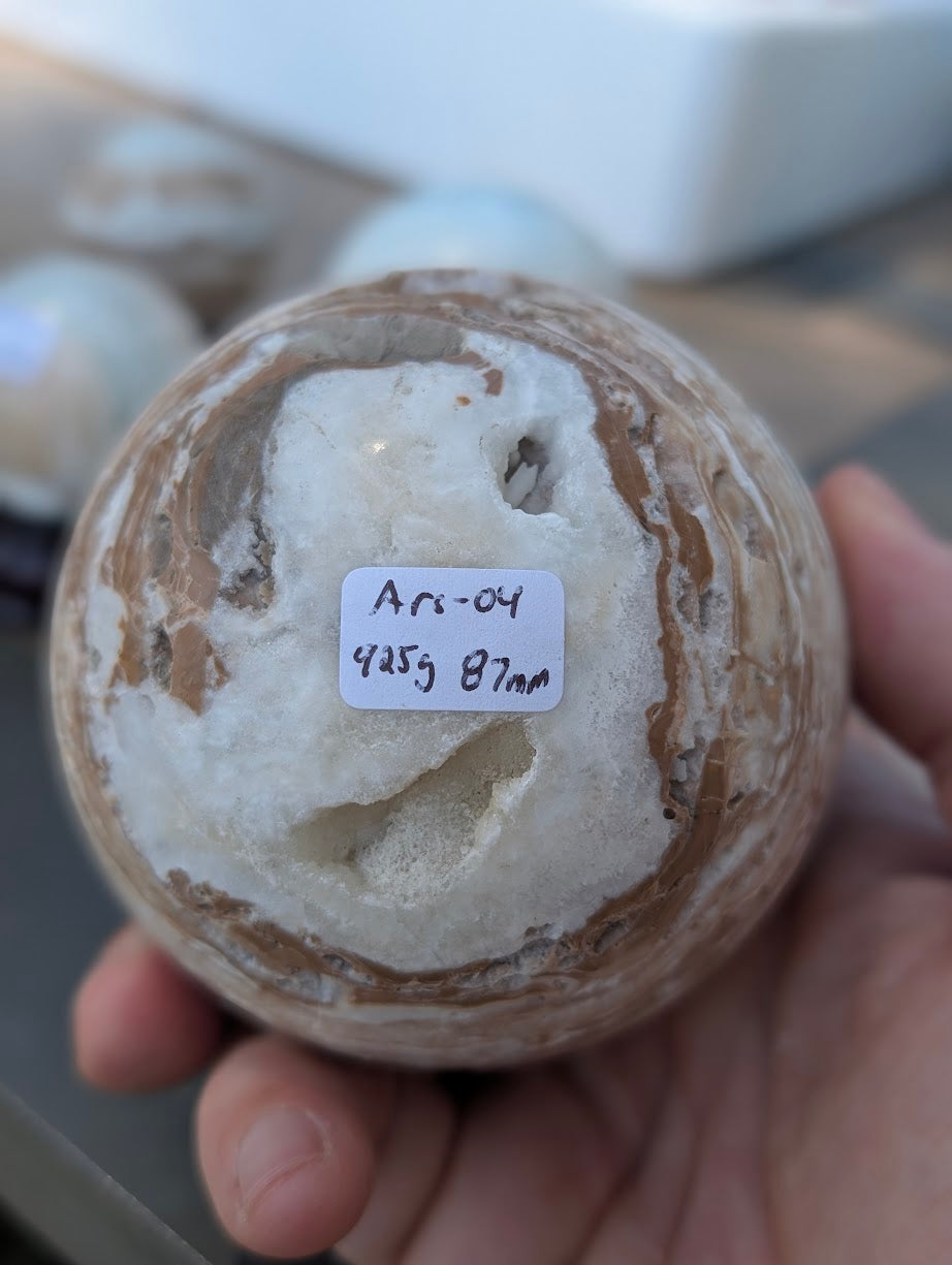 Base view of the 63mm Blue Aragonite sphere held in hand, showing the 350g weight label for variant Ars-04.